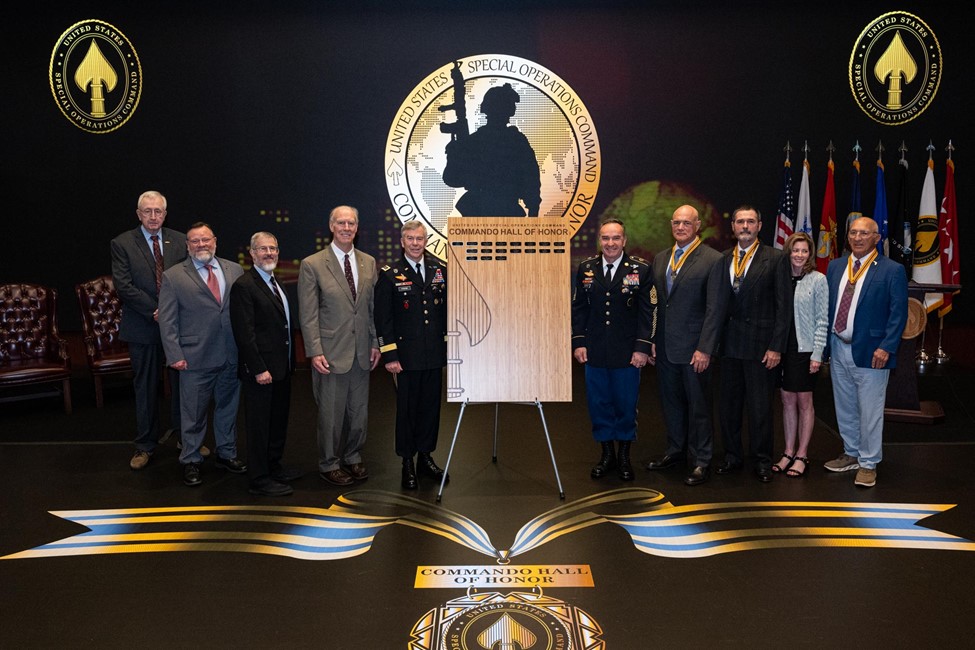 A group of people standing next to a plaque displaying the names of 18 inductees to the Commando of of Honor Ceremony